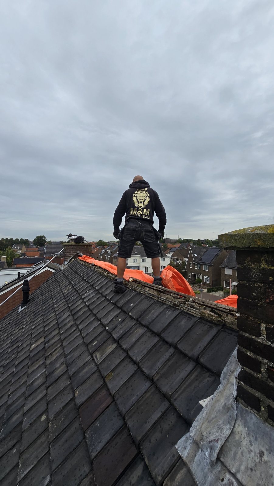 Teamlid in een hoodie met het M&M-logo op een pannendak bij de nok