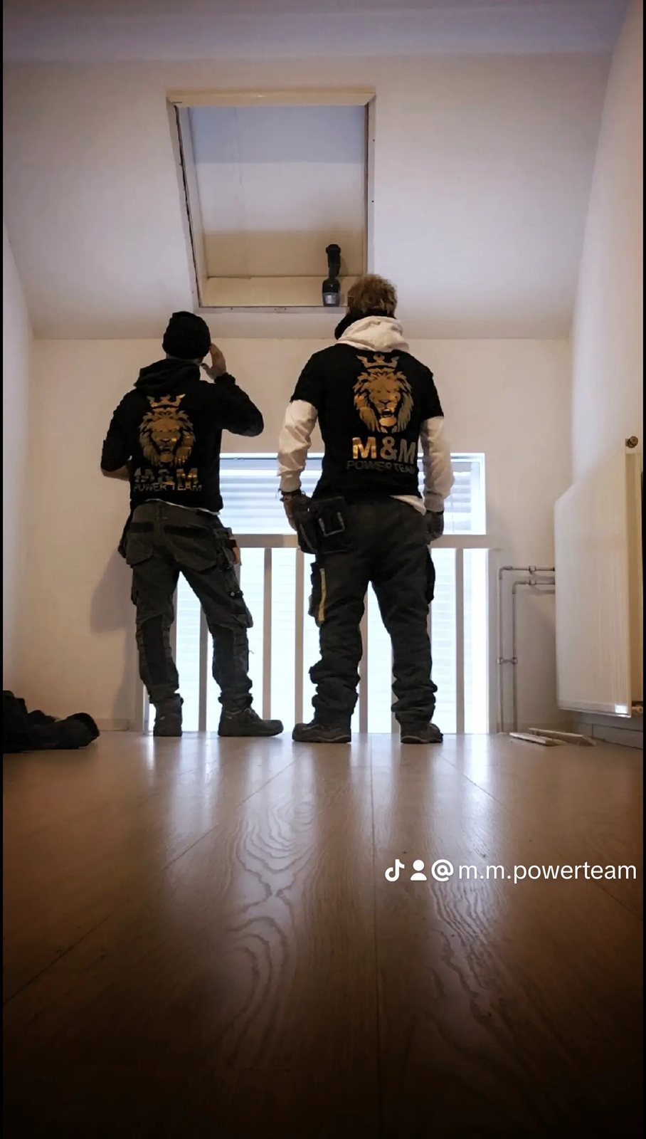 Twee teamleden in shirts met het M&M-logo onder een dakluik in een woning