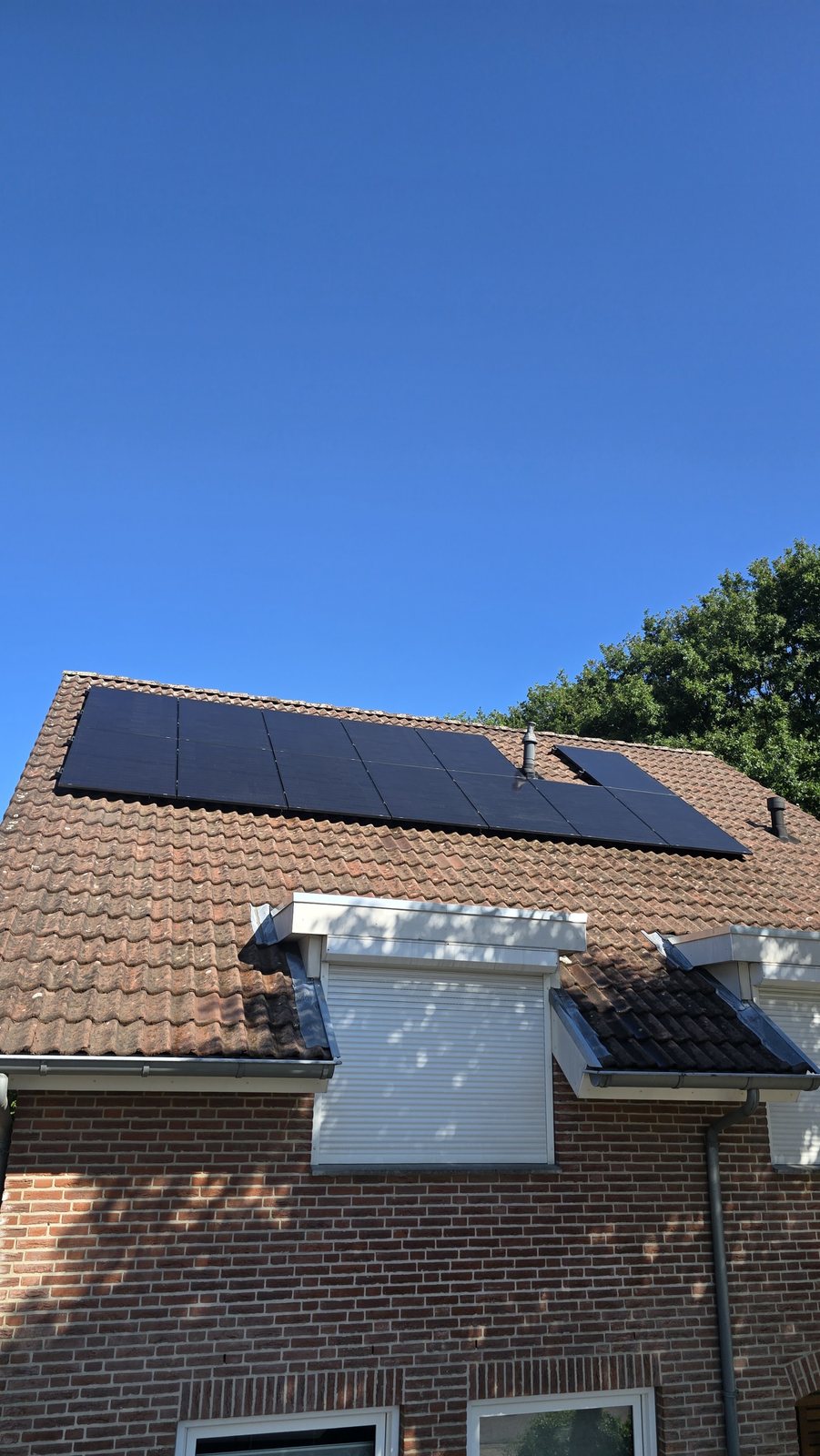 Zonnepanelen op een schuin pannendak onder een blauwe lucht